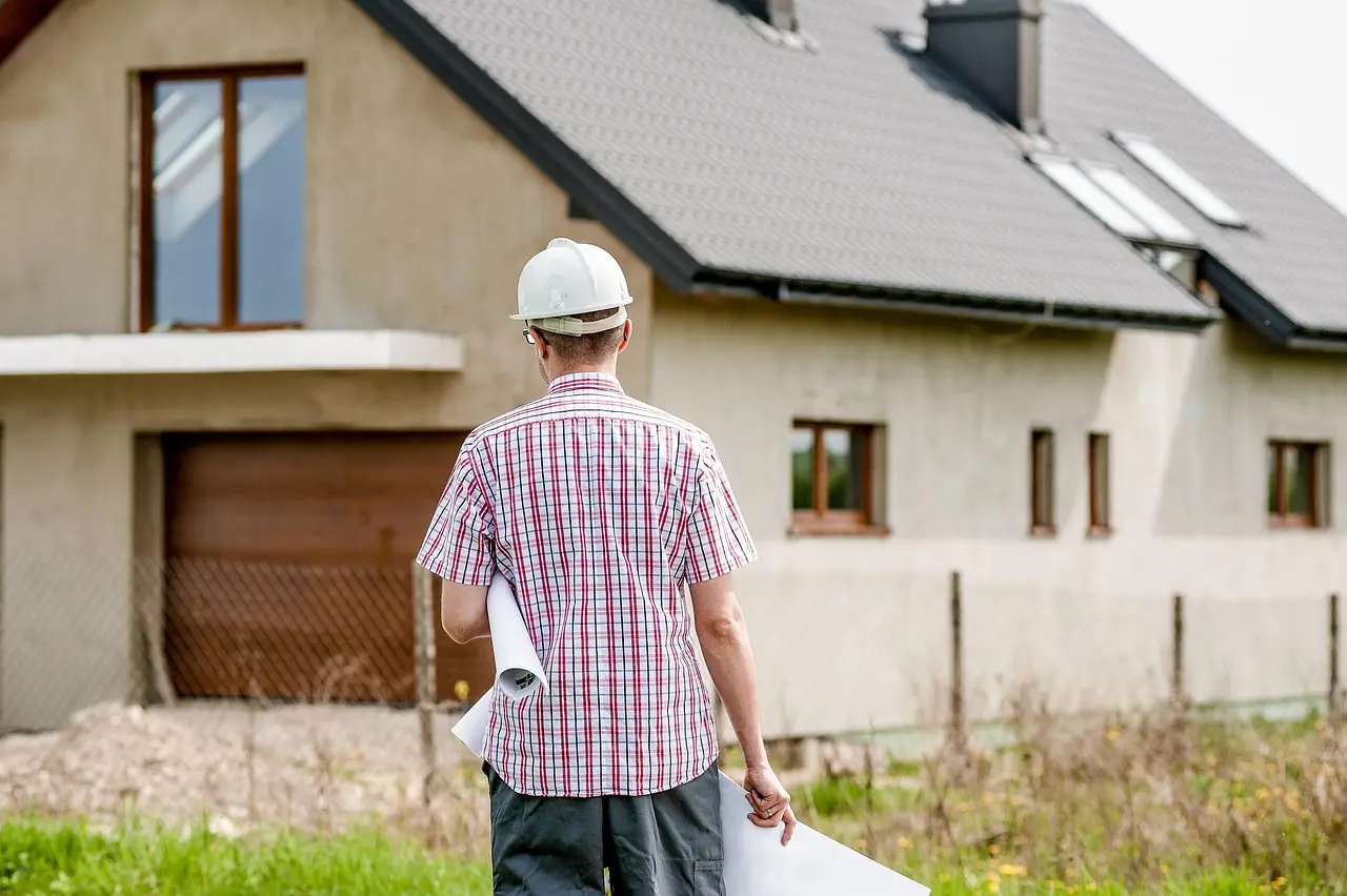 Homme en casque de chantier, plans à la main, devant une maison individuelle